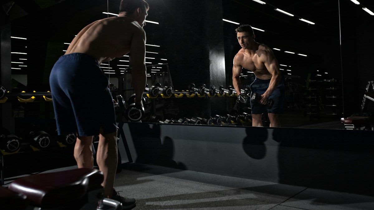 man carrying dumbbell standing in front of mirror